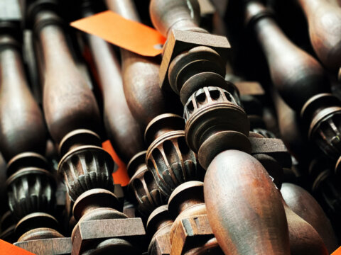 A close-up of intricately carved mahogany balusters stacked together, some with orange tags.