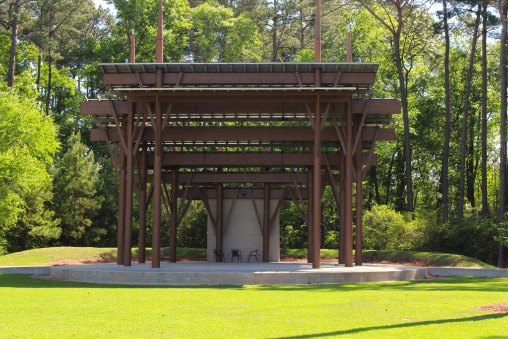 Open-air stage structure surrounded by trees, with two chairs on the platform.