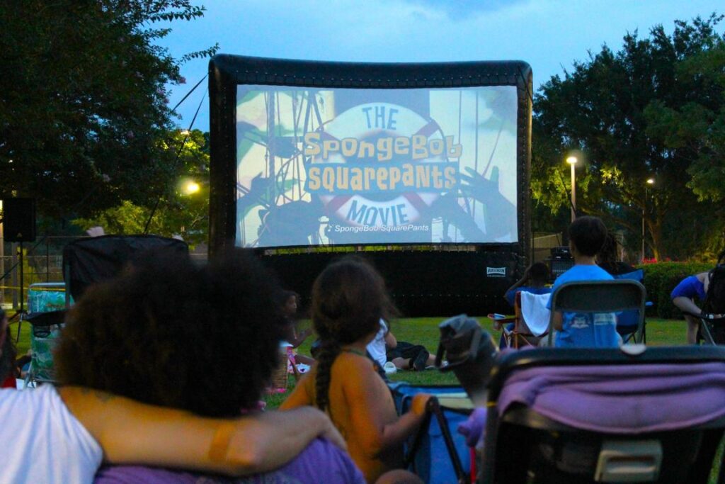People watch "The SpongeBob SquarePants Movie" on a large outdoor screen at dusk.