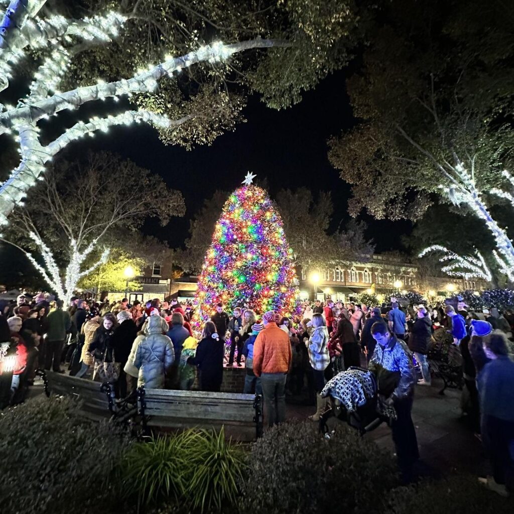 Crowd gathers around a brightly lit Christmas tree in a festive night scene.