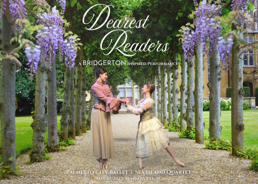 Two dancers in historical costumes hold hands in a garden lined with trees and purple flowers.