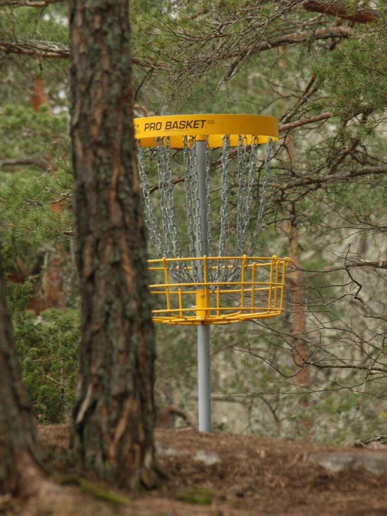 A yellow disc golf basket stands among trees in a forested area.