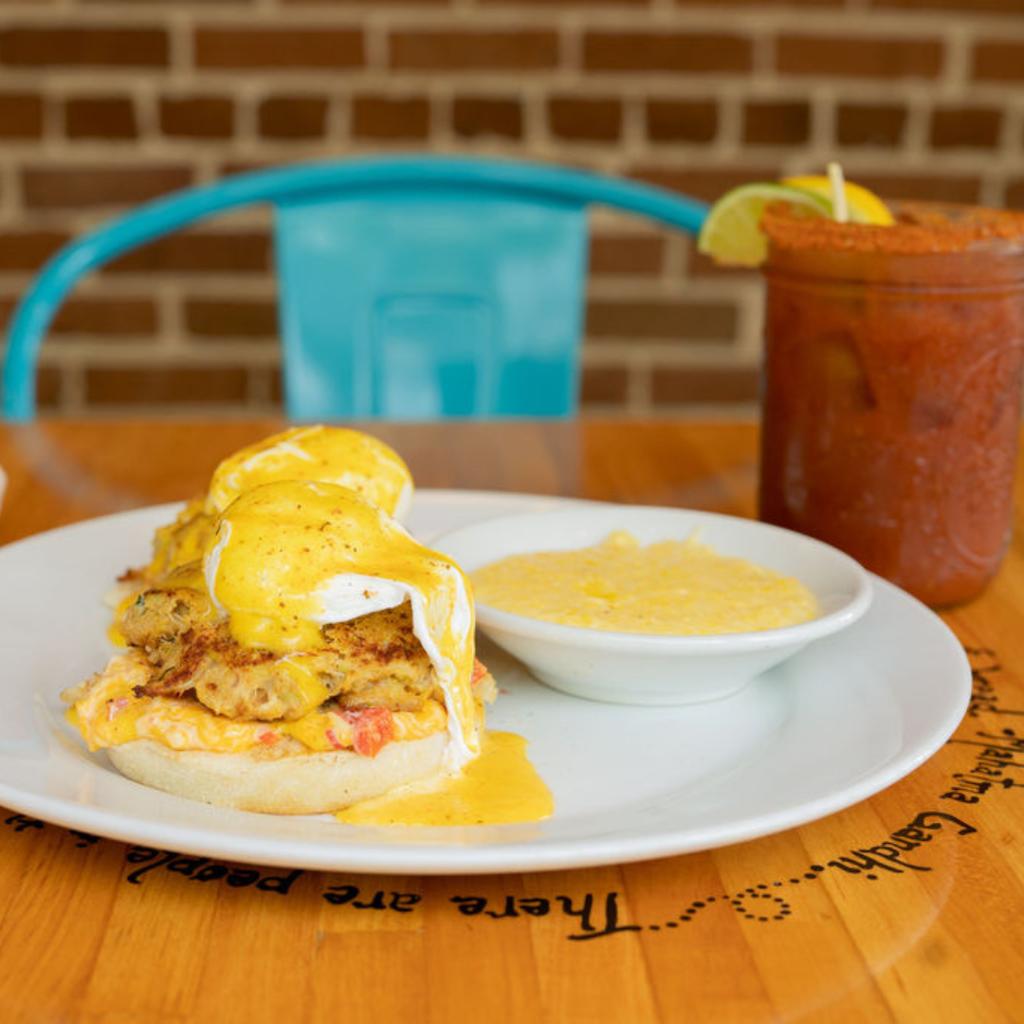 Plate with eggs Benedict on an English muffin, served with grits and a drink in a casual dining setting.