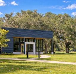 Four musicians stand together outdoors, holding instruments, in front of a brick wall.
