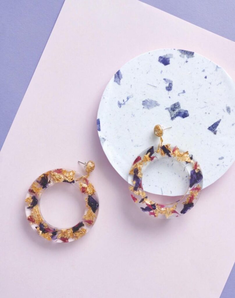 Colorful resin earrings with gold flakes displayed next to a circular decorative plate on pastel backgrounds.