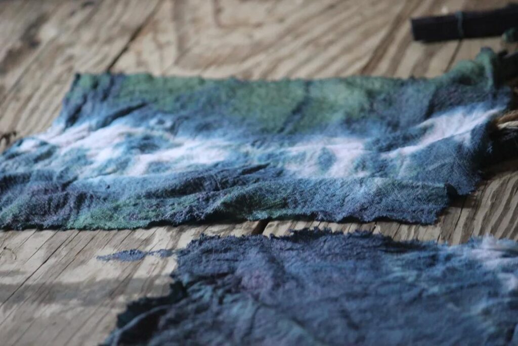 Textured fabric pieces in shades of blue and green laid on a wooden surface.