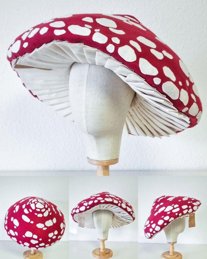 A large, red mushroom-shaped hat with white spots displayed on a wooden stand.