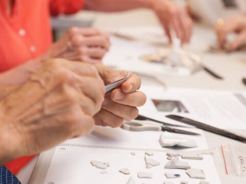 Hands work on small ceramic pieces at a table, focusing on preservation techniques.