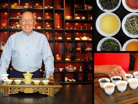 A smiling man stands behind a tea display, showcasing various tea types in cups and a decorative teapot.