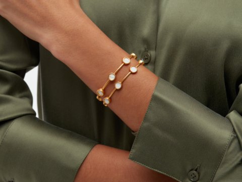 A close-up of a hand wearing a gold bracelet with circular white stones, against a green shirt.