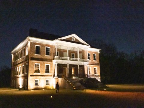 A historic brick house illuminated at night, with a person walking up the steps.
