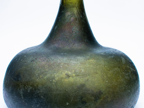 A close-up of a textured, dark green glass vase with a narrow neck and rounded body.