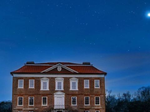 A historic brick building under a starry night sky, with a bright celestial object visible.
